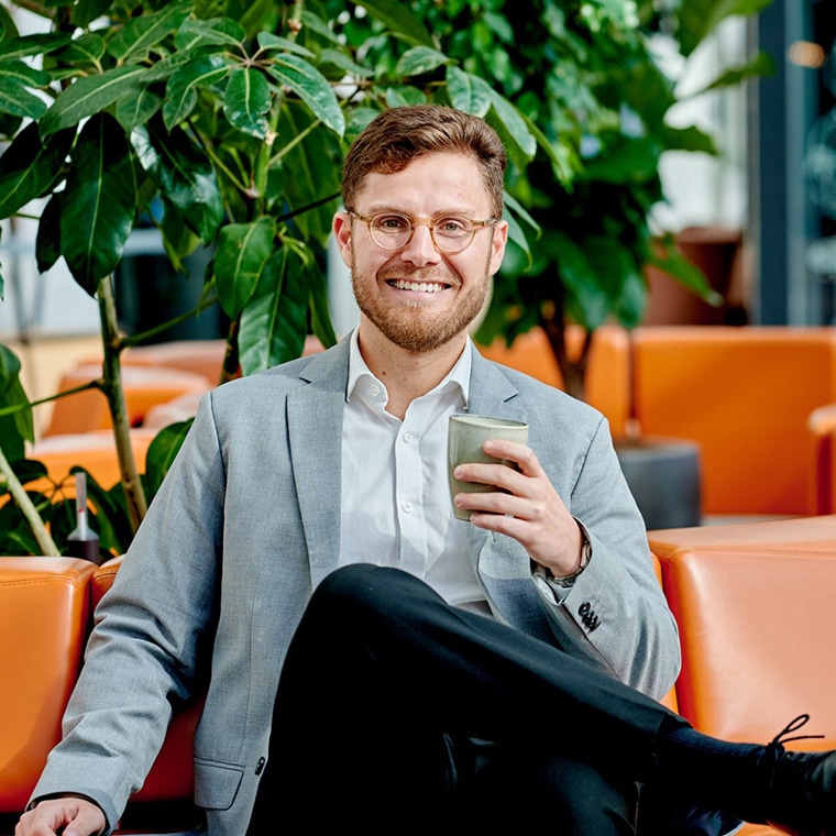 een collega van QISS-IT zit met een kop koffie in zijn hand lachend voor de camera