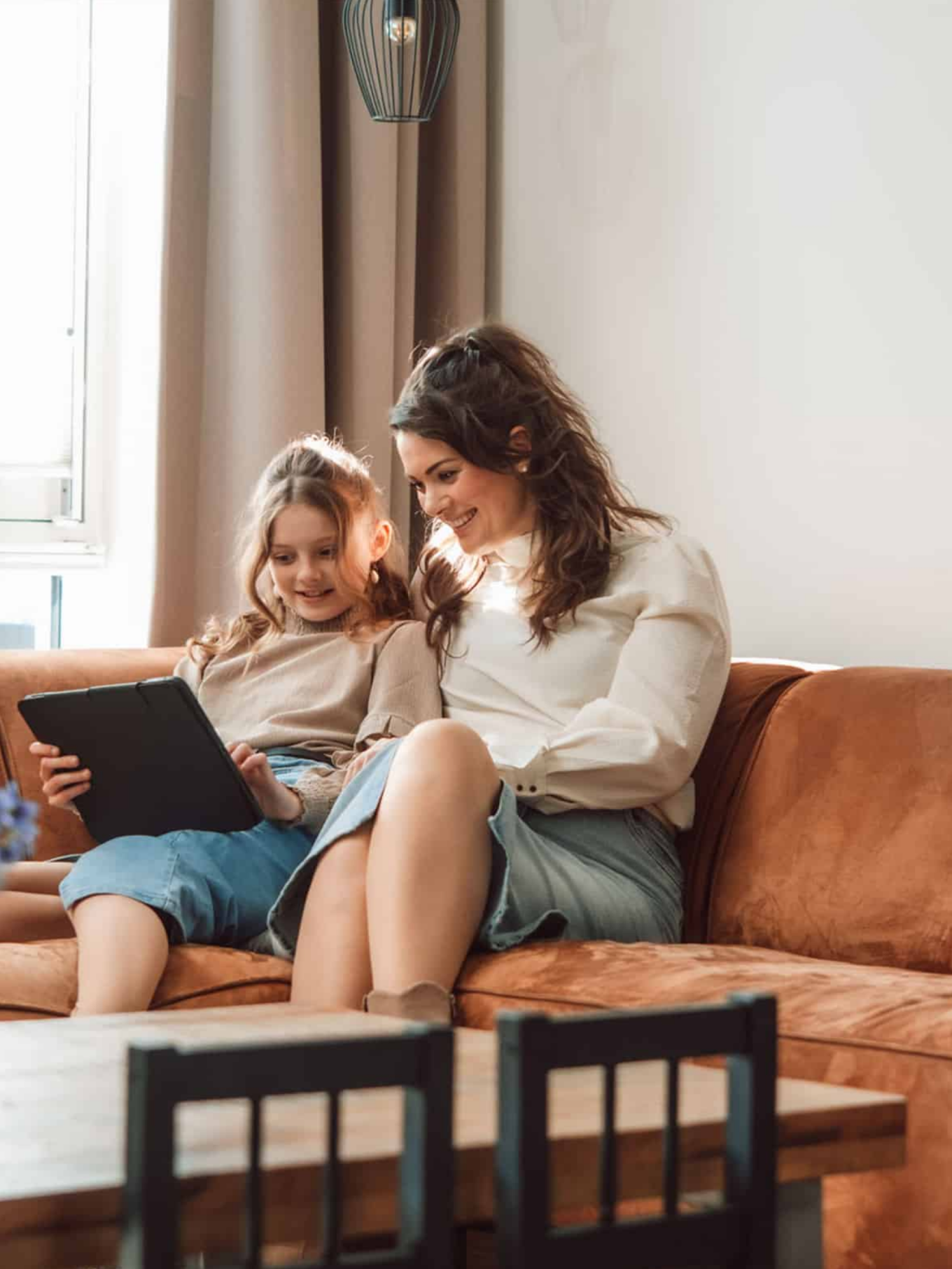 Een moeder en een kind zitten samen met een tablet op de bank en kijken naar het scherm
