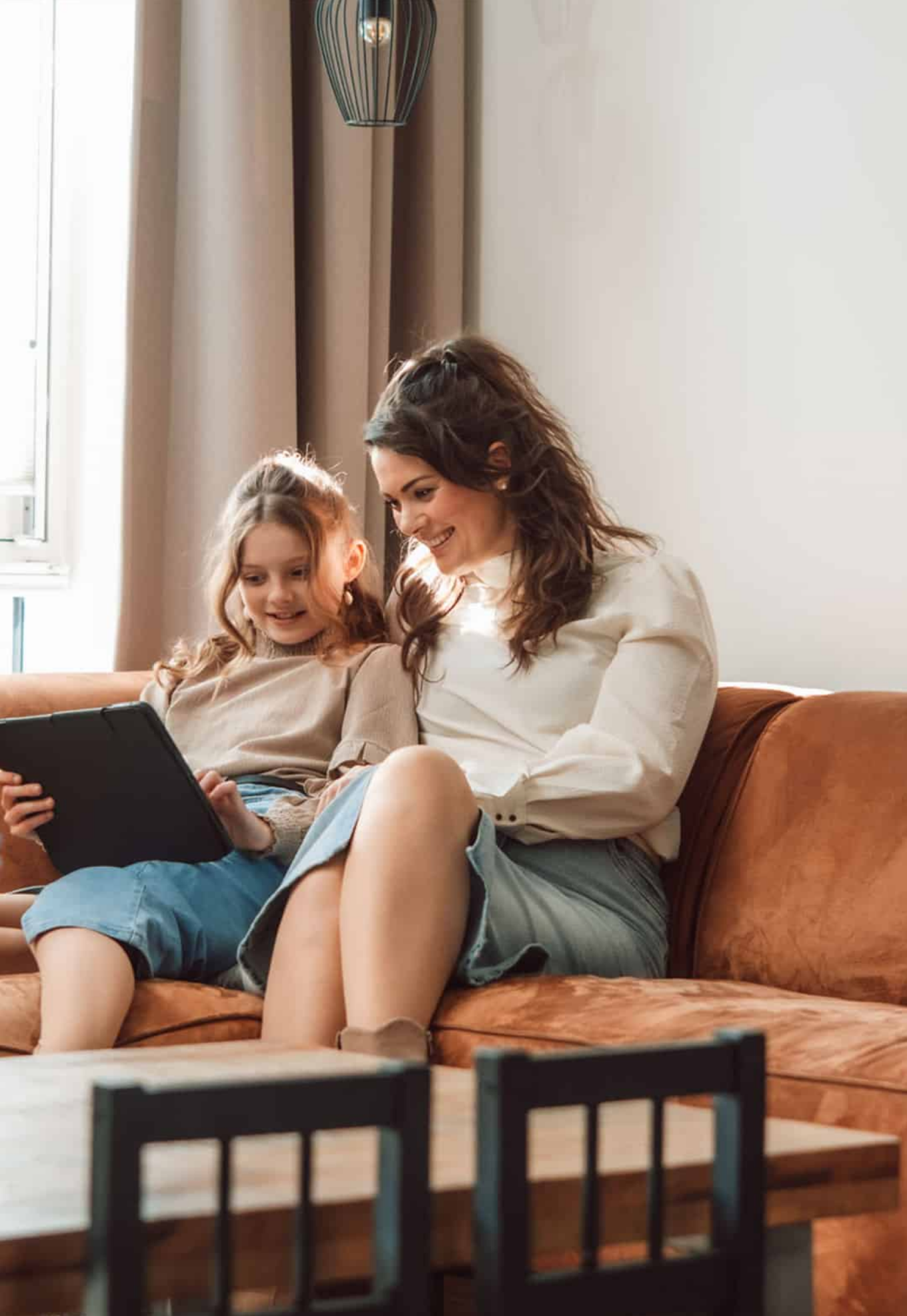 Een moeder en een kind zitten samen met een tablet op de bank en kijken naar het scherm