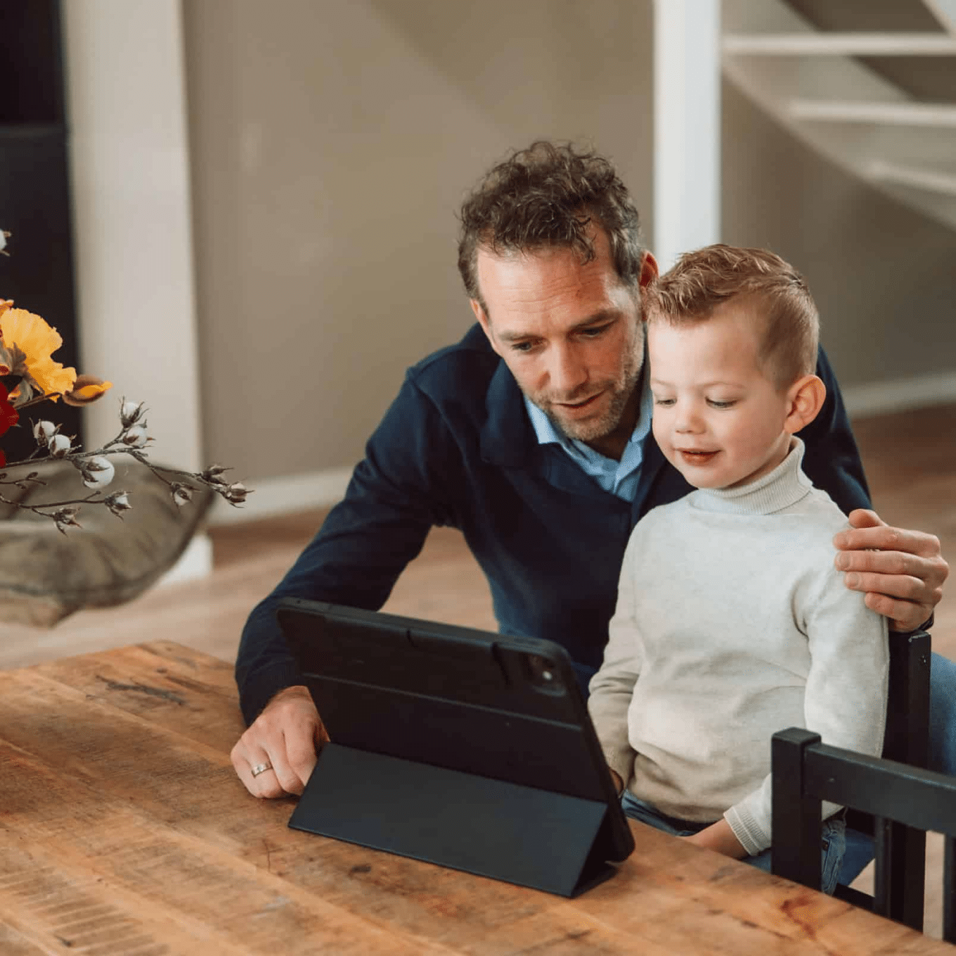 Vader en zoon zitten achter een tabblad en vader laat iets aan zijn zoon zien